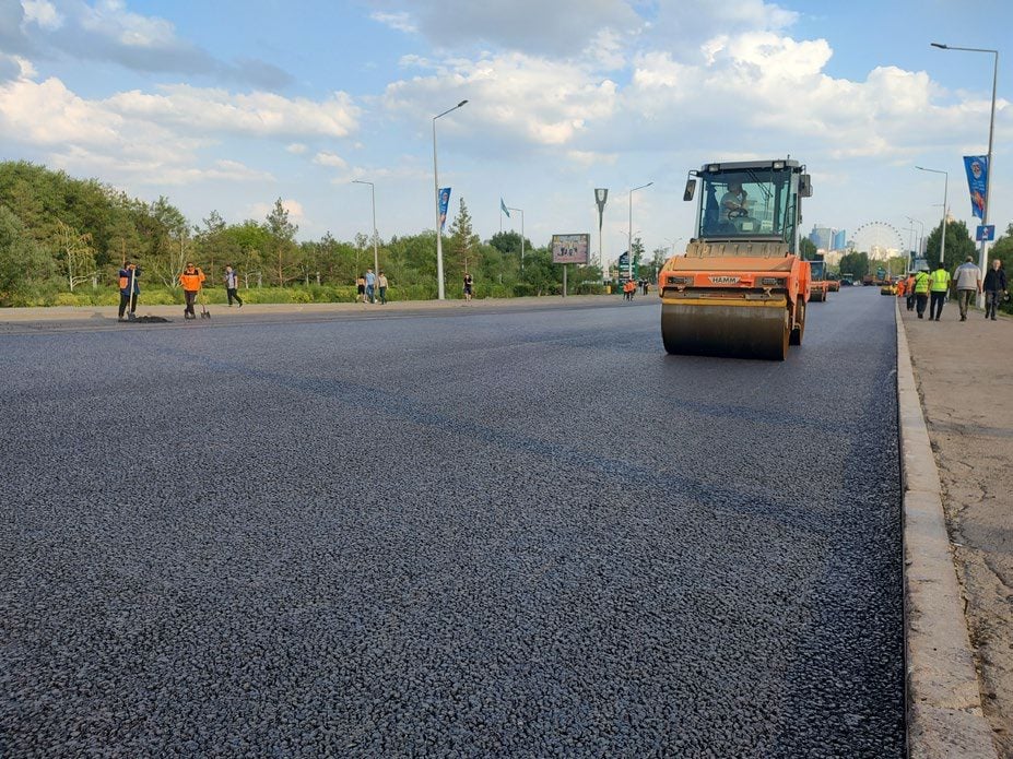 Un compacteur sur une large chaussée fraîchement mise en œuvre, l'équipe sur la section