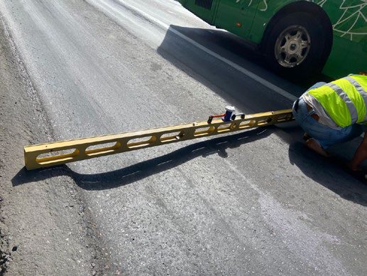 Uma régua sobre a camada fresca, um operário verificando a regularidade na borda do pavimento